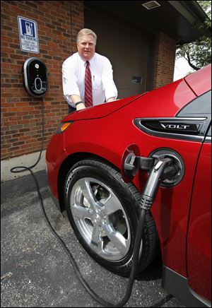 Re/Max Masters Realty broker Jon Modene poses with his Chevy Volt electric automobile as it charges at the electric charging station he has installed at his office in Perrysburg.