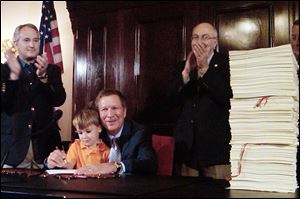 Felix Falco Plouck, 4, the son of a cabinet member, helps Ohio Gov. John Kasich sign the state's two-year budget in Columbus last week. The governor is flanked by state Senate President Keith Faber (R., Celina), left, and House Finance Committee chairman Ron Amstutz (R., Wooster), right.