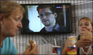 Transit passengers eat at a cafe with a TV screen with a news program showing a report on Edward Snowden, in the background,  at Sheremetyevo airport in Moscow, Russia, on June 26.