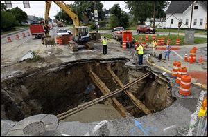 Workers assess the area of the sinkhole July 5, 2013 at the intersection West Bancroft Street and North Detroit Avenue in Toledo