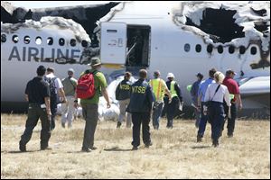 Investigators examine the wreckage at the scene of the Asiana Airline crash Sunday. The Asiana flight crashed upon landing Saturday at San Francisco International Airport, and two of the 307 passengers aboard were killed.