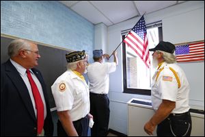 State Rep. Dale W. Zorn of Ida, left, watches as James Walker, commander of the Monroe County Disabled American Veterans; Larry Brossia, of the Sons of American Legion Squadron 72, and Richard Cummings, commander of American Legion Post 72, hang a flag at Dundee Middle School.