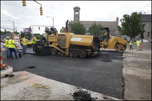 Workers from Ebony Construction Company of Sylvania pave North Detroit Avenue at W. Bancroft Street today. The road reopened today after the sinkhole was repaired.