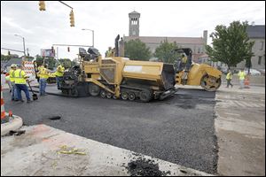 Workers from Ebony Construction Company of Sylvania pave North Detroit Avenue at West Bancroft Street on Thursday.