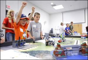 Enzo Mignano, 9, left, Monroe, cheers as he and Erik Seitz, 10, also of Monroe, watch their robot move a block to plug a dam at the Intermediate School District’s robotics camp in Monroe.