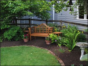 The lawn remains the centerpiece in this yard but was greatly downsized and shaped by a landscaped perimeter consisting of furniture, statuary and a variety of perennials.