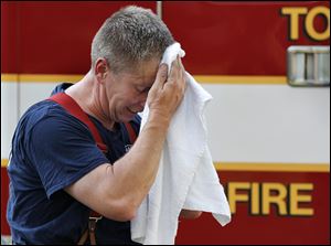 Toledo firefighter Mike DelVecchio wipes sweat from his head after battling a fire at a vacant home at 814 Willow Ave. in East Toledo. Thursday’s extremely hot weather made firefighting’s physical work with heavy, protective clothing even more arduous than usual. 