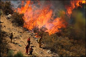 A female inmate hand crew from Puerta La Cruz and firefighters in an engine company with them set fire to reinforce the line to stave off part of the Mountain Fire burning up a hill toward them on Tuesday near Lake Hemet, Calif.