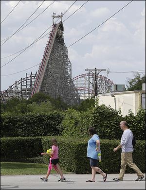 The Texas Giant roller coaster ride sits idle as people walk outside the Six Flags Over Texas park Saturday in Arlington. Investigators will try to determine if a woman who fell to her death from the roller coaster was properly secured by ride operators.