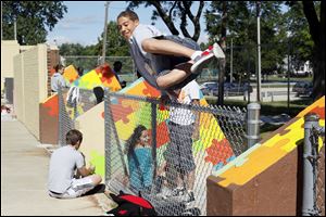Brandon Young, 15, of Toledo hops over a fence while painting in an Arts Commission-sponsored art project at Roosevelt Pool in Smith Park. The painters were turning drab concrete into vibrant rushes of color for the neighborhood.