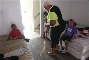 Carlee Carter sweeps the floor to rid it of bugs that infest her home at the Greenbelt Place apartment complex along Cherry Street. Her children, from left, Adron, 3, Shydoria, 7, and Joseph, 8, all sleep in that room to avoid roaches that scurry across the carpet in the upstairs bedrooms.