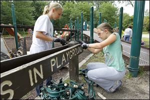 Samantha Hirsch, 11, and her sister Sydney Hirsch, 8, dismantle a playground sign at Pearson Metropark in Oregon. The 11,000-square-foot area will be the site of a larger play­s­cape in the fall.