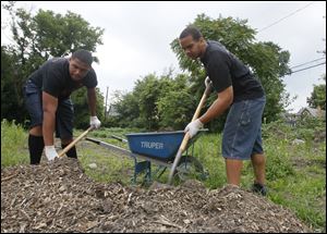 Sophomore Teion Lee, 16, left, and junior Matthew Dunn, 16, both of Woodward High School, load mulch into a wheelbarrow as they help tend the My Brother's Keeper garden.