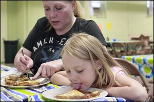 Natalie Fisher helps her daughter, Savannah Scott, 7, eat French toast at Baby University, a series of parenting classes for low-income parents at the South Toledo Community Center.