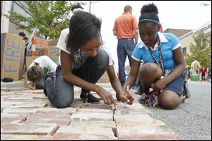 Toledo School for the Arts seventh-graders Ayiana Byrd, left, and Jayla Aimuanvbosa, right, sign their names to bricks at the Toledo Warehouse Association space.
