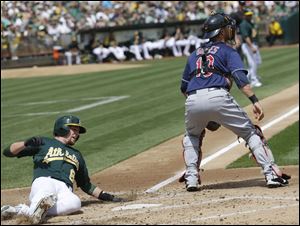 Oakland's Jed Lowrie, left, scores past Cleveland Indians catcher Yan Gomes after a single from Josh Donaldson during the second inning Sunday in Oakland, Calif.