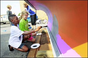 Crim Elementary school students Mozelle Ofori-Atta, left, 9, and Bethany Yoast, 10, right, work on the plows while art teacher Noreen Overholt, back right, explains to Jordan Brenner, left, 9, how to paint the blade that they designed. Painted snow plows from 3 elementary schools and 1middle school will be put on display in the upcoming Black Swamp Arts Festival prior to usage during winter.