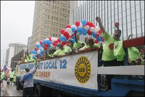 Pete Gerken, president of the Lucas County commissioners and a member of UAW Local 12, shakes hands with a truckload of Local 12 workers on a float in the parade. The event drew thousands of spectators downtown Monday.