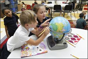 Kashayla Faulkner, left, watches Brittany Taber and Riley Taber find locations on a globe during the Toledo Public Schools/YMCA day-care program at DeVeaux Elementary School in West Toledo.