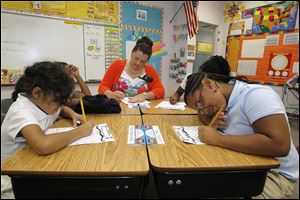 Discovery Academy third grade teacher Barbara Kosch writes  a note for a student’s parents while the students work on an assignment. The children, clockwise from front left, are: Sobeya Abugheneima, Briana Bailey, Aayonah Marshall, and Lynnisha Foster.