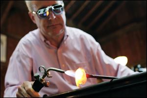 Glass artist Mark Matthews of Wauseon uses a blowtorch help shape a blob of molten glass that will become a marble during a demonstration at Sauder Village in Archbold, Ohio.
