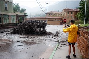 John Shada, of Manitou Springs, Colo., takes a photo of flood water as it shoots out of a sewer on Canon Avenue on Thursday in Manitou Springs, Colo.