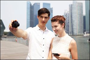 A couple use Sony's QX100 camera to take a photo of themselves. The camera offers a variety of features, from a real shutter button to stero microphones to a memory-card slot and more.