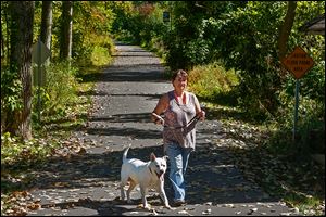 Chris Bowes of Ottawa Lake walks her dog Artie along the River Trail in Harroun Park in Sylvania. The first phase of the trail was finished last year, and officials are discussing its path across hospital land.