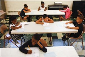 Jose Carrizales, 8, center, smiles at Diego Duran, 8, right, as they work on a reading-writing skill packet during a tutoring session at Monroe United Methodist Church in Toledo. 