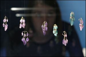 A museum employee poses by pendants with bunches of carved amethyst and emerald grape seen on display in an exhibition 'The Cheapside Hoard: London's Lost Jewels' at the Museum of London.