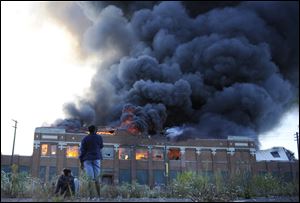 Onlookers watch as a large plume of smoke rises above a warehouse building on Detroit's west side on Sept. 26.
