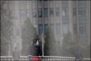 A woman wearing a face mask looks at the traffic as she bicycles on a road in Beijing today.