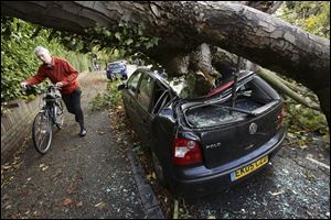 A car is crushed under a fallen tree as a man pushes a bicycle nearby following a storm, in Hornsey, north London.