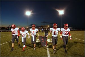 Bedford senior Jeremy Harris (90), Lucas Mayo (21), Boss Brad (2), Alec Hullibarger (11), and Jack Maison (35) carry their teammate Colton Durbin's number three jersey off the field before the start of the match up between Monroe Jefferson and Bedford Friday.