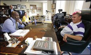 Dallas King, 18, right, sits in Mayor Mike Bell’s chair Tuesday at One Government Center in Toledo. The Whitmer High senior, who has cerebral palsy, recently made a a PowerPoint presentation for his classmates about his skydiving adventure.