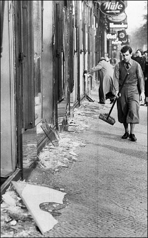 A young man with a broom prepares to clean away broken window glass from a Jewish shop in Berlin the day after Kristallnacht, Nov. 9, 1938.