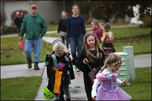 Katelyn Feltz, 6, left, peeks in her bag as she and Chloe Erickson, center, join trick-or-treaters in Bed-ford Township. Unlike several area communities, Bedford did not cancel trick-or-treat Thursday.