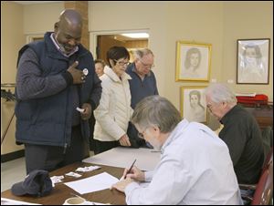 Toledo mayor Mike Bell applies a voting sticker after signing in to vote. Behind him are Tess, center, and Chris McDonnell, both of Toledo.