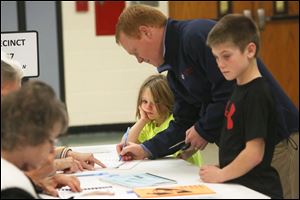 Kate Walendzak, 6, center, waits with her brother Connor, 9, right, as their father, Dan, center, signs in before voting at the Fort Meigs Elementary polling location in Perrysburg.