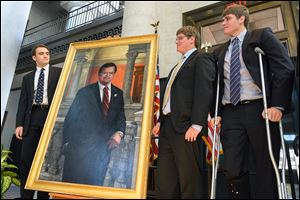 Paul Michael, left, Adam, and Connor Gillmor stand with the official portrait of their father, ex-Senate President Paul Gillmor, during a Statehouse ceremony on Tuesday. Toledo artist Leslie Adams painted the portrait that will hang in the Senate Caucus room.
