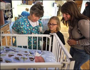 Allison Herr, 10, of Metamora, looks at a baby in the neonatal intensive care unit at Mercy St. Vincent Medical Center with nurse Cheryl Thacker, left, and her mother, Jenny Herr.