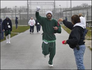 Toledo Correctional Institution prisoner Steve James lifts his arm in celebration of completing another lap during a 5K fund-raiser for the Susan G. Komen Foundation. He is reaching for a wristband from Case Manager Terrie Janowski to mark his laps.