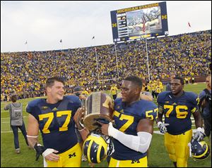 Taylor Lewan, left, and Frank Clark carry the Little Brown Jug after defeating Minnesota. Lewan is a likely first-round NFL pick.