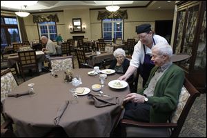 Residents Betty Regan and Russ Fitts are served dinner by Elane Kelley in the dining room of St. Clare Commons.