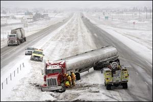 A tanker truck is tended to by firefighters after sliding off the snowy highway near mile marker 48 on Interstate 90 in Piedmont, S.D. Tuesday.