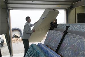 Volunteers Jeremy Litchfield, left, and Mike Torres move a mattress at the Sauder warehouse. Mr. Torres, touched by the program’s generosity when he moved to Archbold from Texas a year ago, said he wanted to give back to others. 