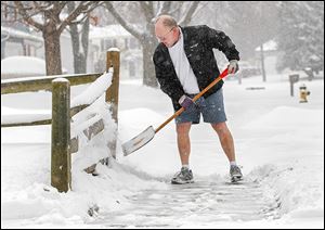 Ken Dreeze shovels his sidewalk in Maumee — in shorts. After all, winter is still a week away.  Temperatures though will remain in the mid-20s today, and 30 mph winds are expected.