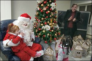Isabella Mason, 3, talks with Santa Claus while Family House Executive Director Reneé Palacios and Breelyn Jeffers, 2, look on. Chrysler’s Toledo Machining Plant employees recently delivered hundreds of gifts to children at the shelter.