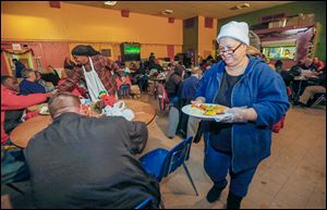 Volunteer Shelley Carithers serves a plate to Adam Gross, left, during a Christmas meal at the Cherry Street Mission in Toledo. About 350 dinners were prepared for the event, a tradition at the mission.