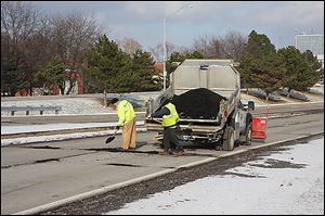 A city crew patches potholes Thursday on the Anthony Wayne Trail near I-75 on the approach to downtown Toledo.
